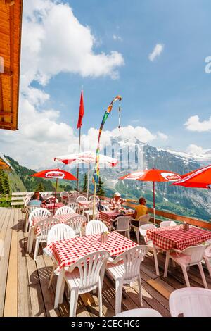 Mountain restaurant with red umbrella sunshades in First, Grindelwald, with view over valley towards the Wetterhorn Stock Photo