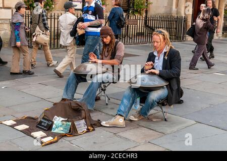 A couple of street buskers with their musical instruments playing to visitors queuing outside the Roman Baths in Abbey Churchyard in the Roman city of Stock Photo