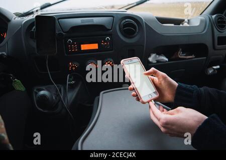 Crop shot of Woman on passenger's seat in car charging smartphone with cable while traveling. Stock Photo