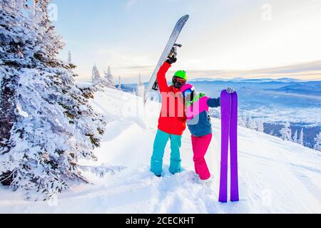 Snowboarder man and woman skier hugging and having fun on background of winter forest and snow. Sunlight in mountains Stock Photo