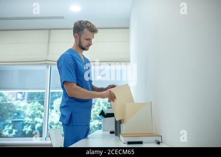 Bearded young doctor putting envelope in standing file folder Stock Photo