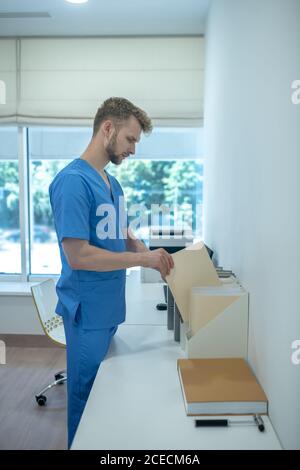 Bearded young doctor putting papers in standing file folder Stock Photo