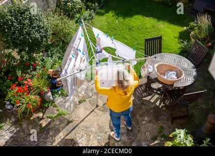Woman hanging out her washing on rotary dryer washing line in small back garden town house in Brighton Stock Photo