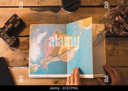 Crop shot from above of person reading maps on table with photo camera and coffee. Stock Photo