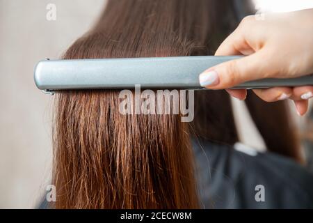 Close up hands of professional hairdresser beauty salon, straighteners curling female hair Stock Photo