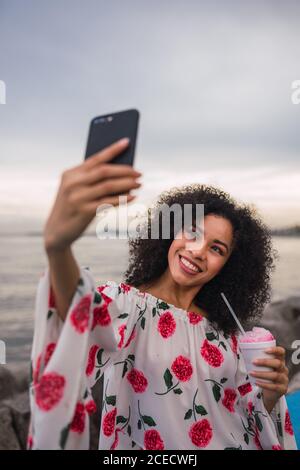 Woman with phone and drink taking selfie on waterfront Stock Photo