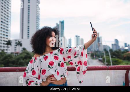 Pretty ethnic Woman in stylish outfit taking selfie happily on background of cityscape, Panama Stock Photo
