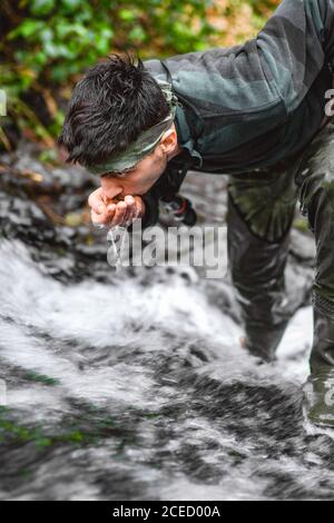 Soldier or revolutionary member or hunter in camouflage near the stream drinking natural clean water from the stream Stock Photo