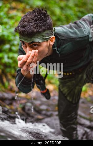 Soldier or revolutionary member or hunter in camouflage near the stream drinking natural clean water from the stream Stock Photo