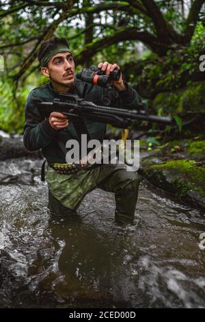 Inside the stream, soldier or revolutionary member or hunter in camouflage, gun in his hand Stock Photo