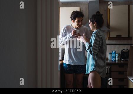 Cheerful young couple standing with cup of coffee on the kitchen in the morning. Stock Photo