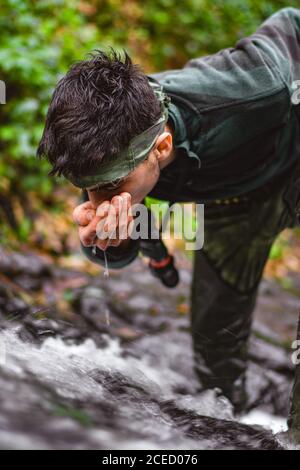 Soldier or revolutionary member or hunter in camouflage near the stream drinking natural clean water from the stream Stock Photo