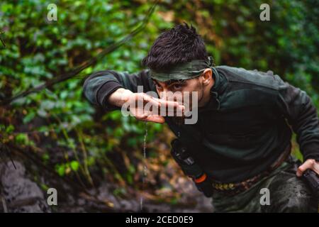 Soldier or revolutionary member or hunter in camouflage near the stream drinking natural clean water from the stream Stock Photo