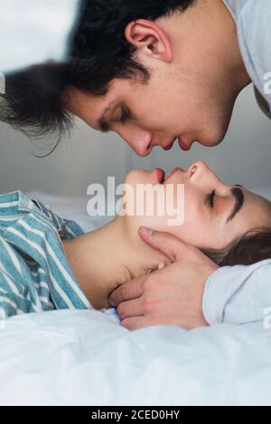 Side view of tender young man and Woman in pajamas lying and bonding on bed. Stock Photo