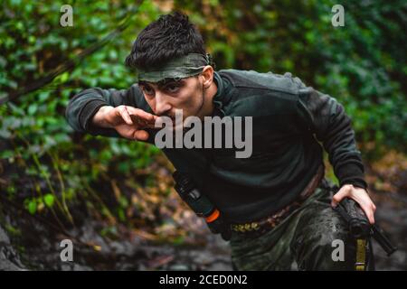 Soldier or revolutionary member or hunter in camouflage near the stream drinking natural clean water from the stream Stock Photo