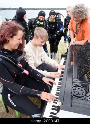 31 August 2020, Saxony, Leipzig: On the beach of the Kulkwitzer See in front of the diving school Delphin, the 15-year-old pianist Florian shows his group of sport divers from Ulm/Neu-Ulm (Baden-Württemberg/Bavaria) and diver Selina Schwarz from Leipzig (front right) different keystrokes on an old grand piano from 1880 which is placed outside. During a festival lasting several days, the 4th Leipzig Keyboard Days (until 13.09.20), a total of ten pianos and grand pianos sponsored by institutions and companies will be on display at various locations in the large new building area. The musical ins