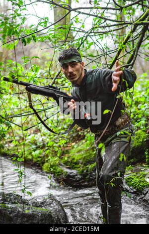 Soldier or revolutionary member or hunter in camouflage in the river observing the gun in his hand Stock Photo