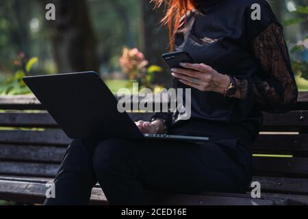 Woman using laptop and smartphone on bench Stock Photo