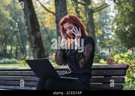 Woman using laptop and smartphone on bench Stock Photo
