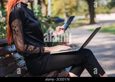 Woman using laptop and smartphone on bench Stock Photo