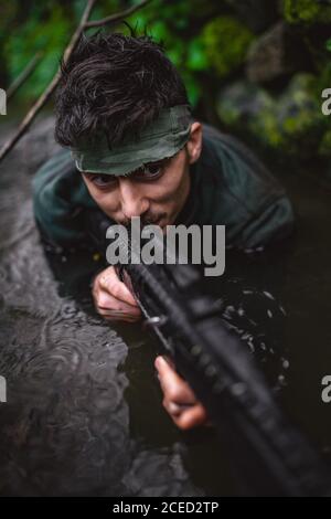 Soldier or revolutionary member or hunter aiming with gun in his hand in camouflage in the river, hunt concept Stock Photo