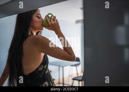 Side view beautiful passionate brunette Hispanic Woman in dress looking away and holding mug of hot drink Stock Photo