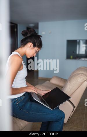 Beautiful brunette Hispanic Woman typing on laptop and sitting on a settee Stock Photo