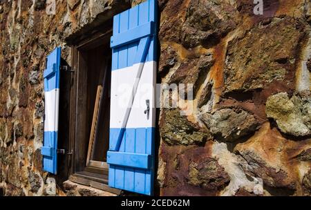 An open window with white and blue wooden shutters of a mountain retreat with stone walls in the Alps (Trentino, Italy, Europe) Stock Photo