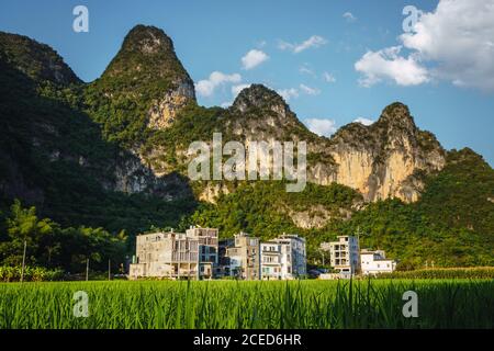 Picturesque view of rice paddy and buildings of small Chinese town placed at bottom of high beautiful mountains on bright sunny day in Guangxi province Stock Photo