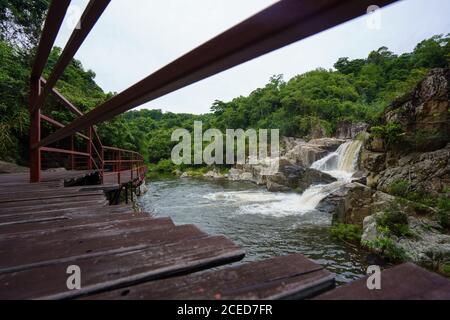 View of small waterfall among rocks in Yanoda Rainforest with wooden walkway on side, China Stock Photo