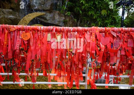 White fence with plenty of hanging bright red wish ribbons in on green trees background in Phoenix Park, Sanya, China Stock Photo