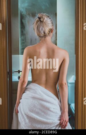 back view of Charming young Woman wrapped in white towel while standing in bathroom doorway after shower Stock Photo