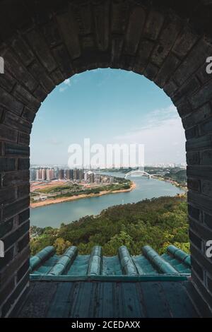 Shot through brick old window with view of cityscape of Nanning on river shore, China Stock Photo