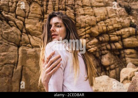 Side view of young Woman sitting and looking at camera at rough rock. Stock Photo
