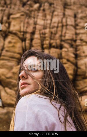 Side view of young Woman sitting and looking at camera at rough rock. Stock Photo