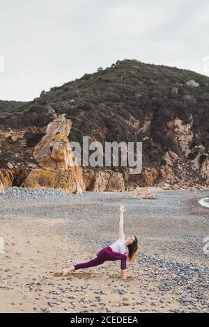 Side view of young Woman doing exercise and stretching on shore at the ocean. Stock Photo