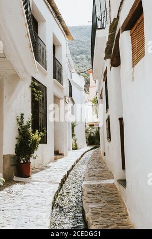 Small water channel going through narrow ancient street on sunny day in Granada, Spain Stock Photo