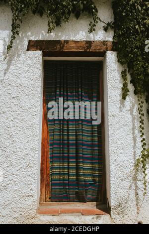 Curtain with striped pattern hanging on window of aged building on sunny day in Granada, Spain Stock Photo
