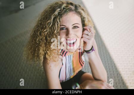 Portrait of beautiful young curly Woman with bright lips smiling cheerfully at camera sitting outdoors Stock Photo