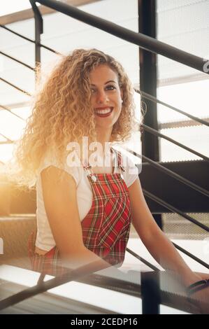 Wonderful young curly Woman smiling at camera on stairs in sunshine Stock Photo