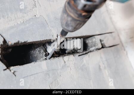 Builder worker man using jackhammer to drill into construction wall for duct for air conditioning pipes Stock Photo