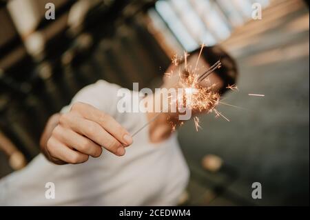 Young handsome man in white T-shirt standing inside building and holding burning Bengal light in hand Stock Photo