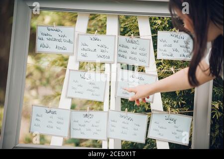 Crop view of young dark haired Woman pointing at note hanging on board with wedding wishes for just married couple Stock Photo