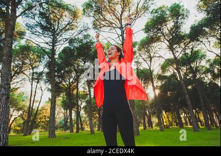 From below of smiling happy Woman in sportswear looking super excited while standing in green park Stock Photo