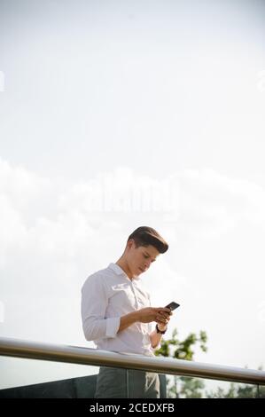 Young man with smartphone leaning on railing Stock Photo