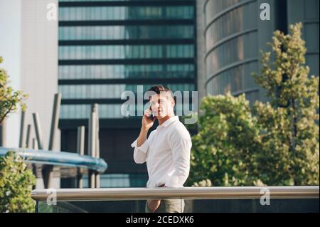 Young man with smartphone leaning on railing Stock Photo