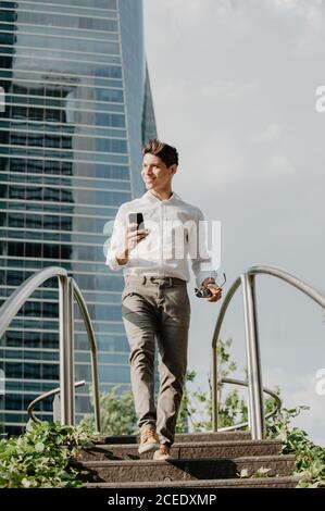 Cheerful man with smartphone walking down steps Stock Photo