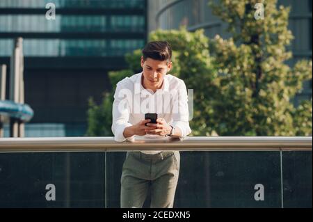 Young man with smartphone leaning on railing Stock Photo