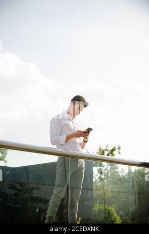 Young man with smartphone leaning on railing Stock Photo