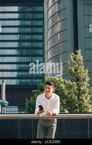 Young man with smartphone leaning on railing Stock Photo